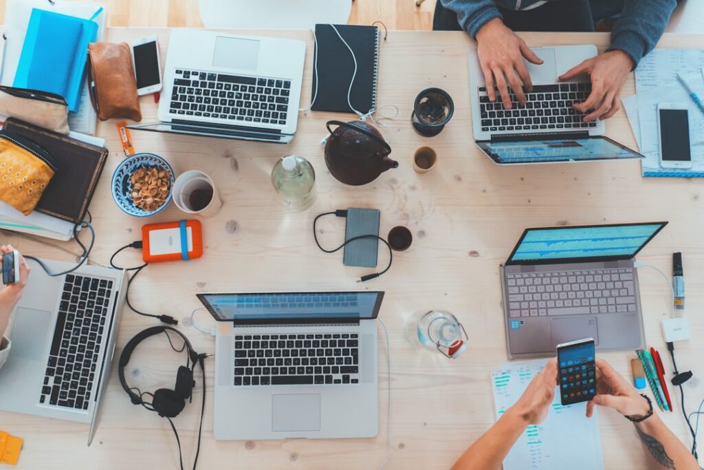 Laptops, notebooks, and coffee on a shared work table, seen from above